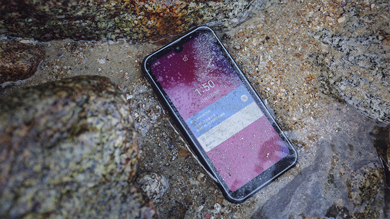 Phonemax rugged smartphone lying wet on a rocky shoreline with its display on